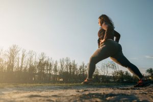 Overweight female standing and stretching with one leg behind her in runner’s pose and hands on hips