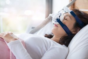 A woman laying on her back in bed wearing a CPAP mask