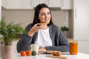 A woman eating toast in the kitchen with food around her