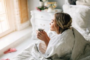 A woman laying on her stomach in bed holding a coffee cup