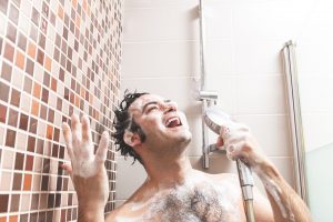 Young Caucasian man, singing and gesturing happily full of soap in the bathroom shower.